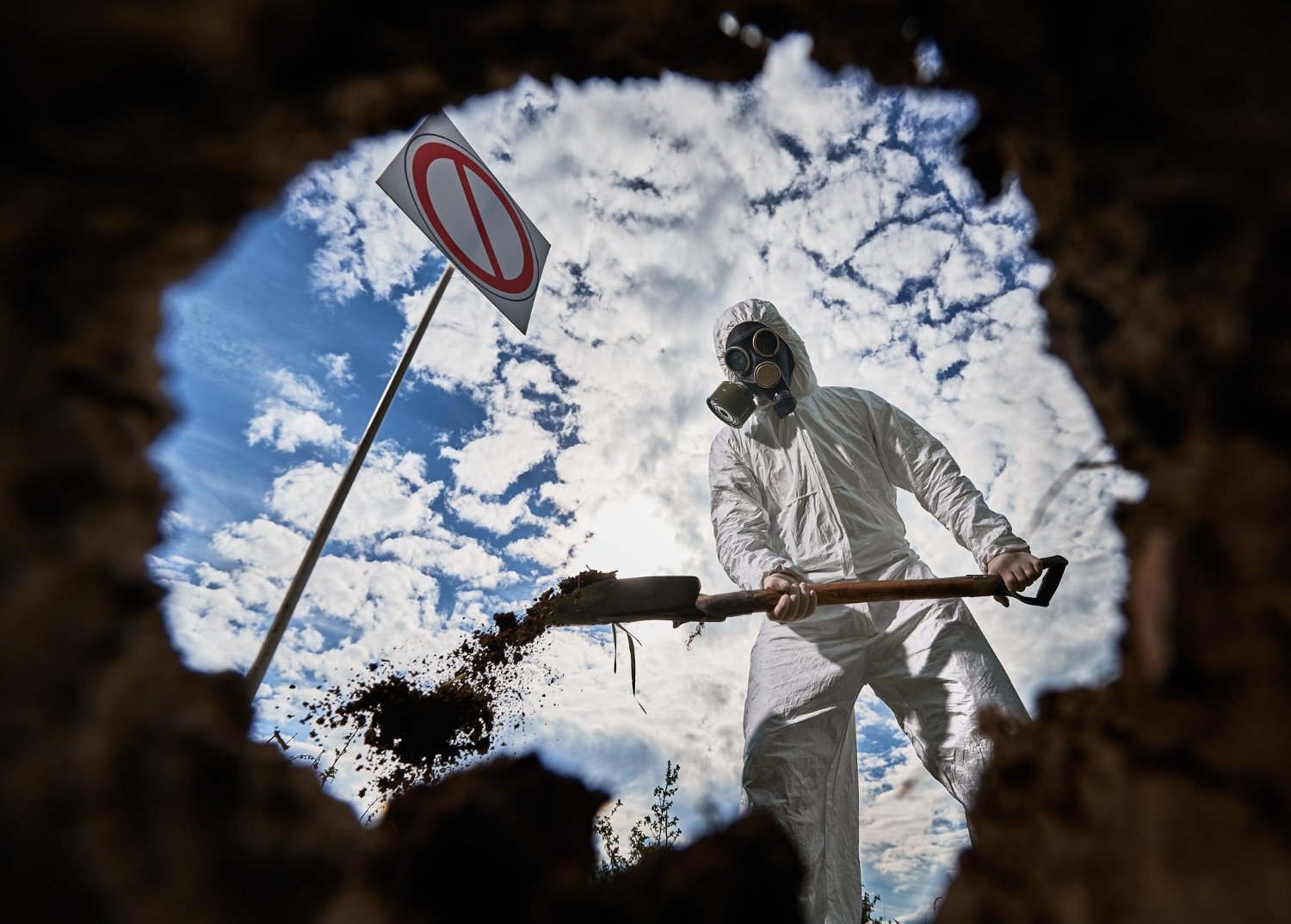 Looking up from hole at hazmat suited worker with shovel